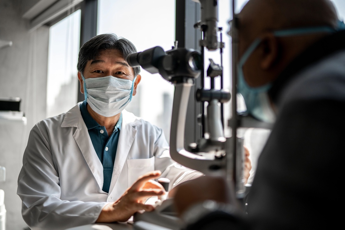 Eye care professional, in lab coat and mask, during eye examination