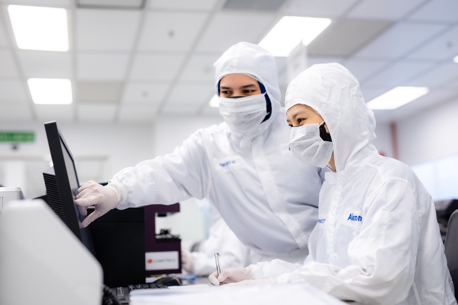 Lab employees in protective clothing looking at computer screen