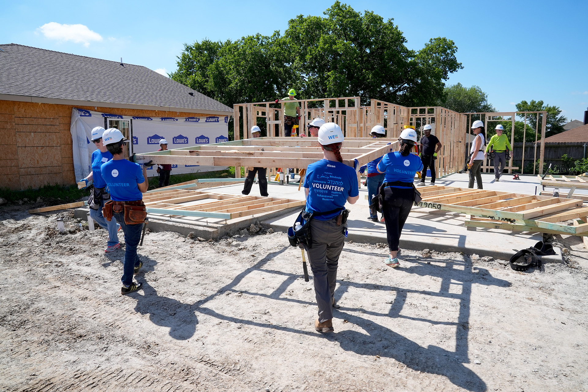 Alcon volunteers in blue t-shirts carrying a wall frame to house being built