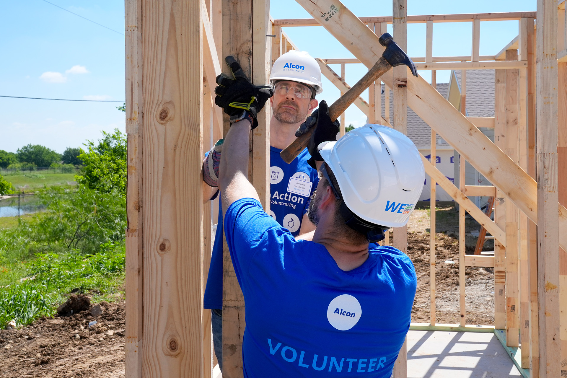 Two Alcon volunteers hammering a board to house frame