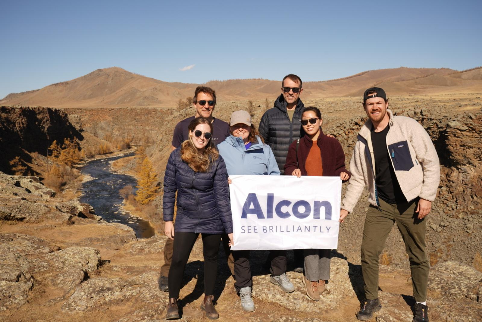Alcon volunteers standing in group outside, holding sign that says "Alcon - see brilliantly"