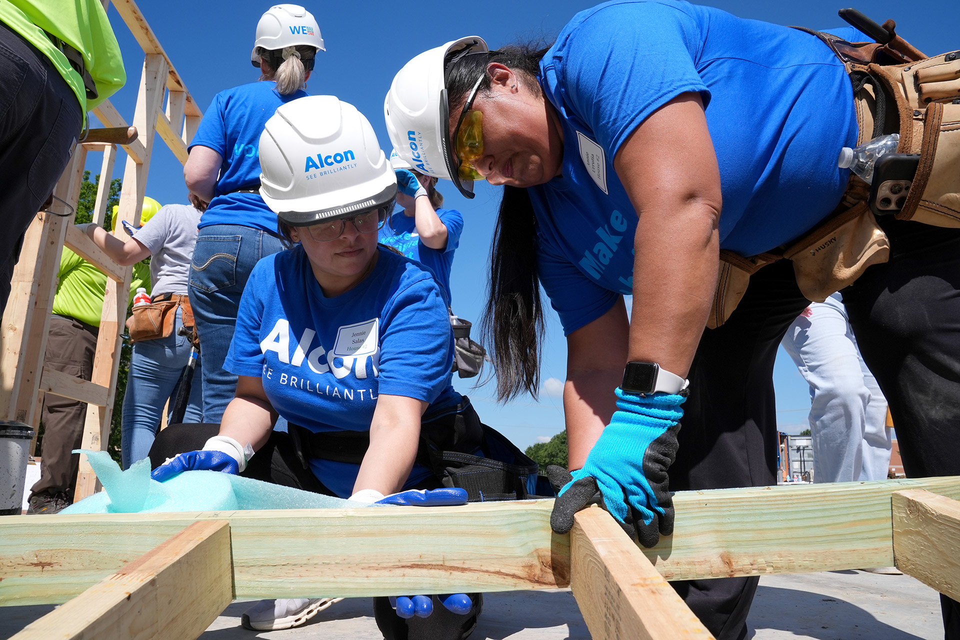 Closeup of Alcon volunteers in blue shirts helping to build the frame of a new home
