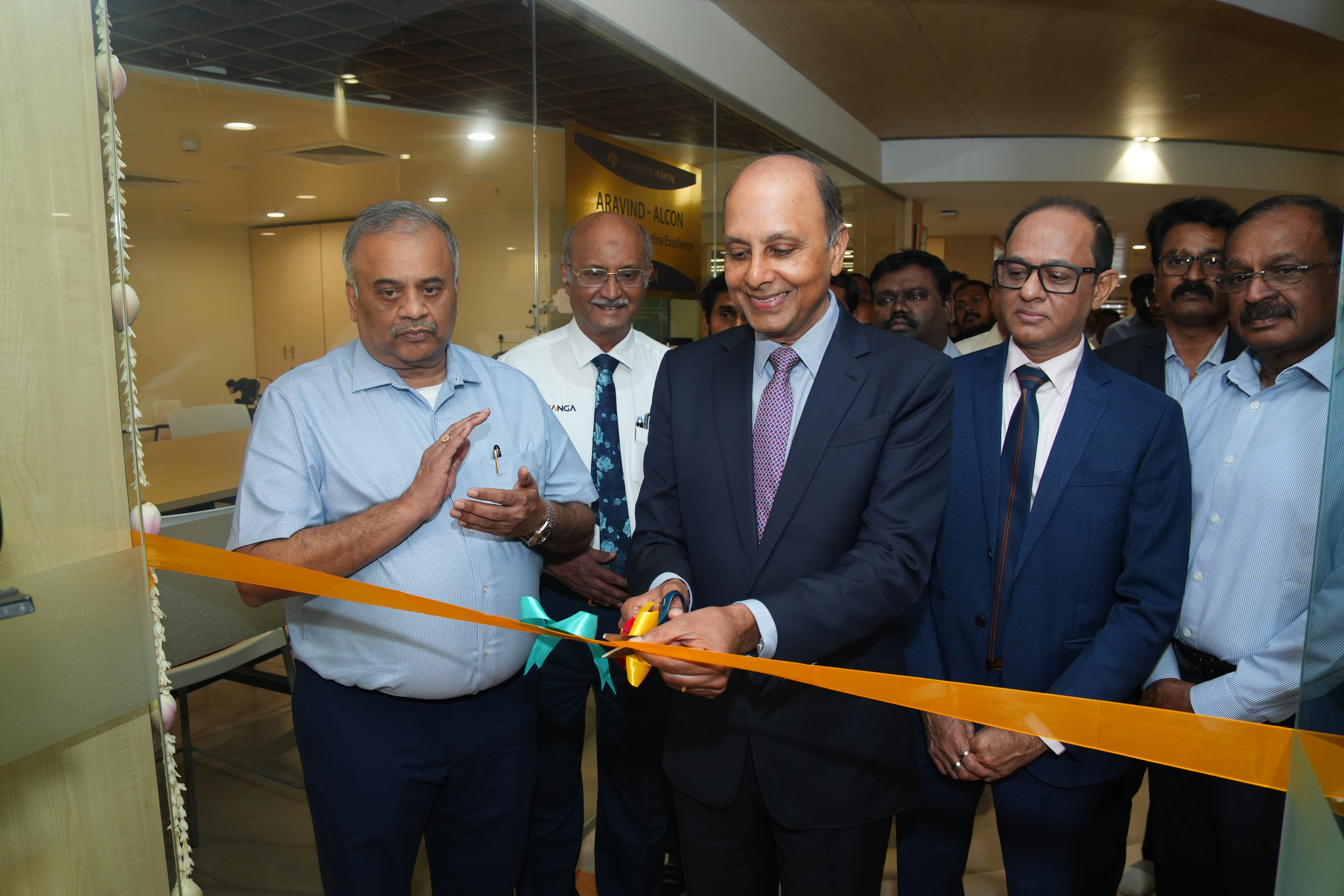 Five men in business dress smiling. One is cutting a ribbon on the new Aravind Retina Centre of Excellence