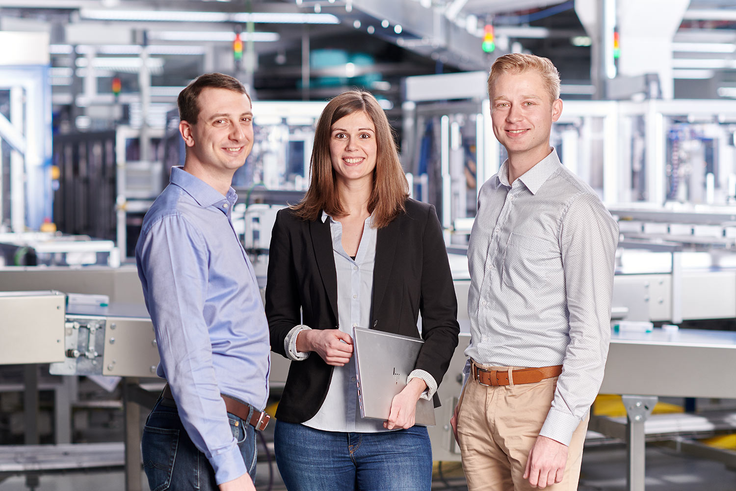 Drei Mitarbeiter stehen in einer Produktionsstätte zusammen und lächeln.