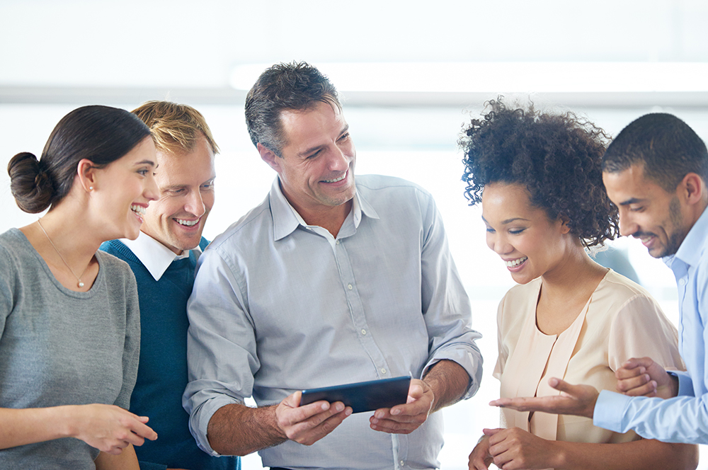 A diverse group of five people are standing in a circle, facing each other and laughing. They appear to be in a casual meeting or workshop setting.