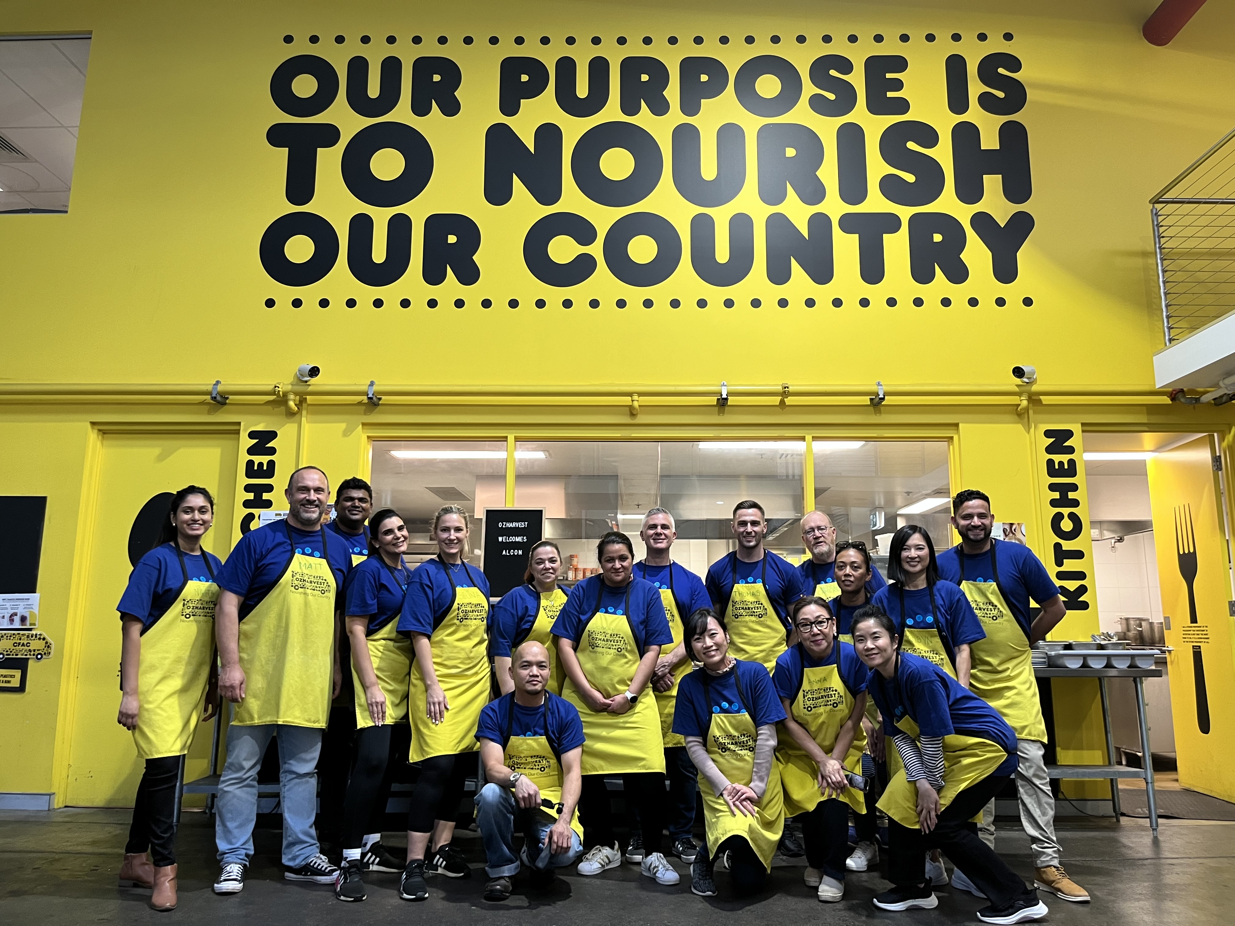 Alcon volunteers with yellow aprons standing in front of signage that says Our Purpose is to Nourish our Country