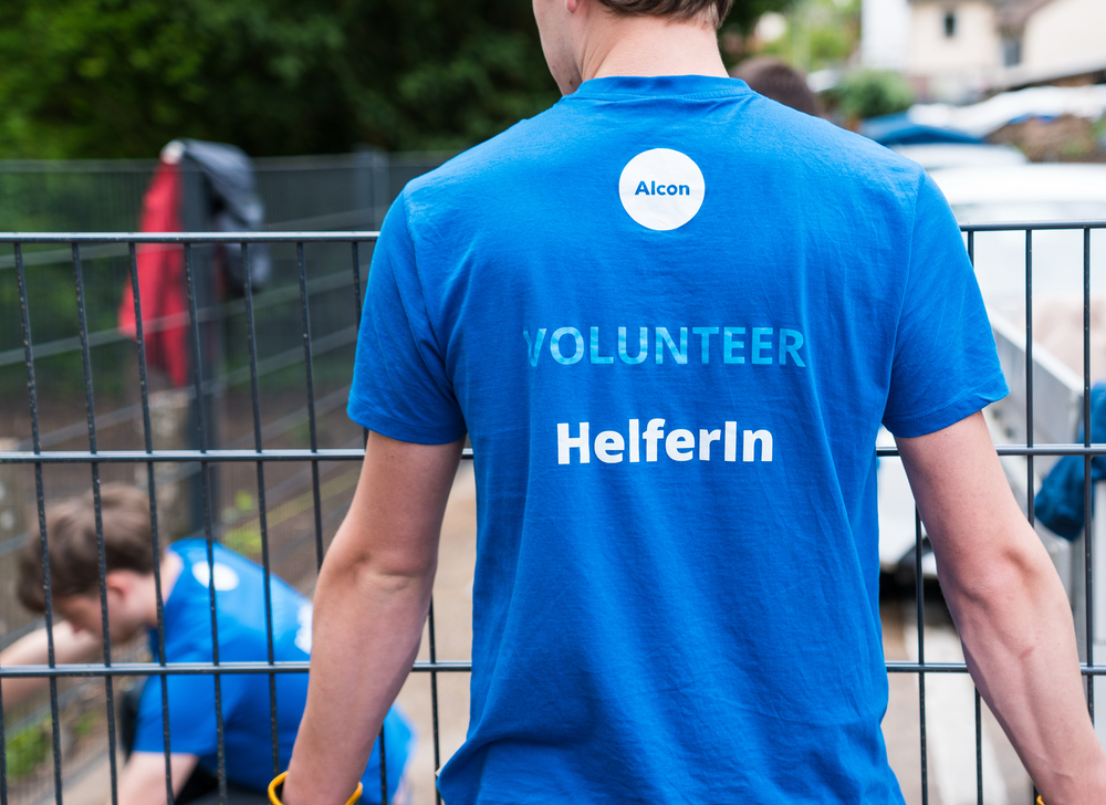 Ein Alcon-Freiwilliger steht mit dem Rücken zur Kamera, um die Rückseite seines blauen T-Shirts für Freiwillige zu zeigen.