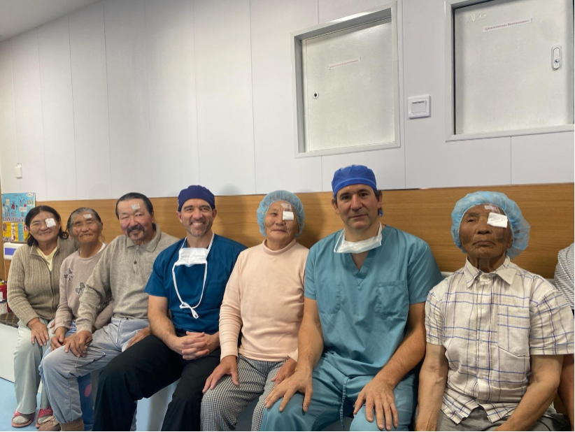 Patients with bandaged eyes and medical professionals sit together on bench