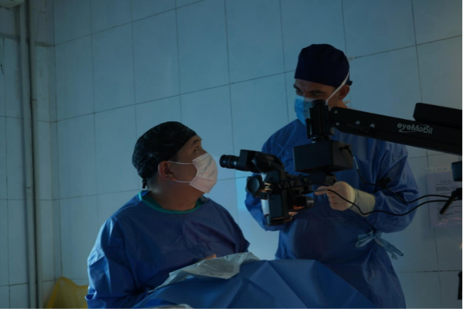 Two medical professionals in surgical gear converse during an eye surgery