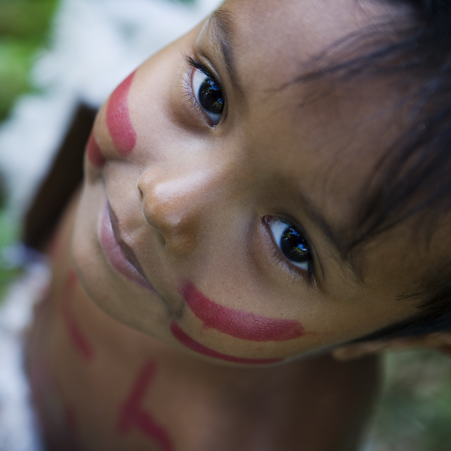 Young child with red face and body paint looks up at the camera