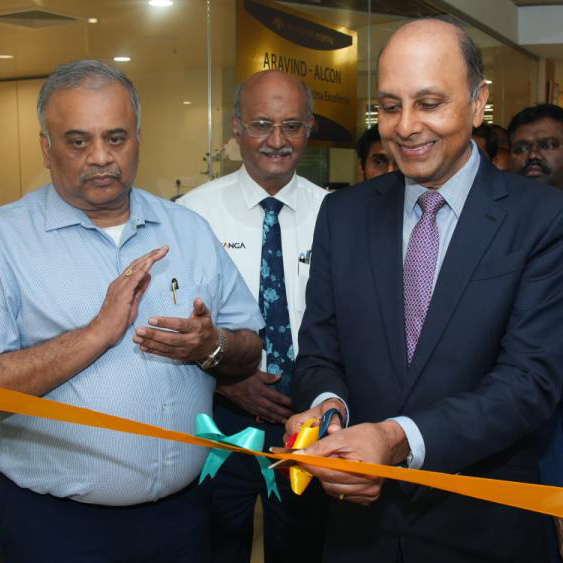 Three people cutting an orange ribbon with scissors.