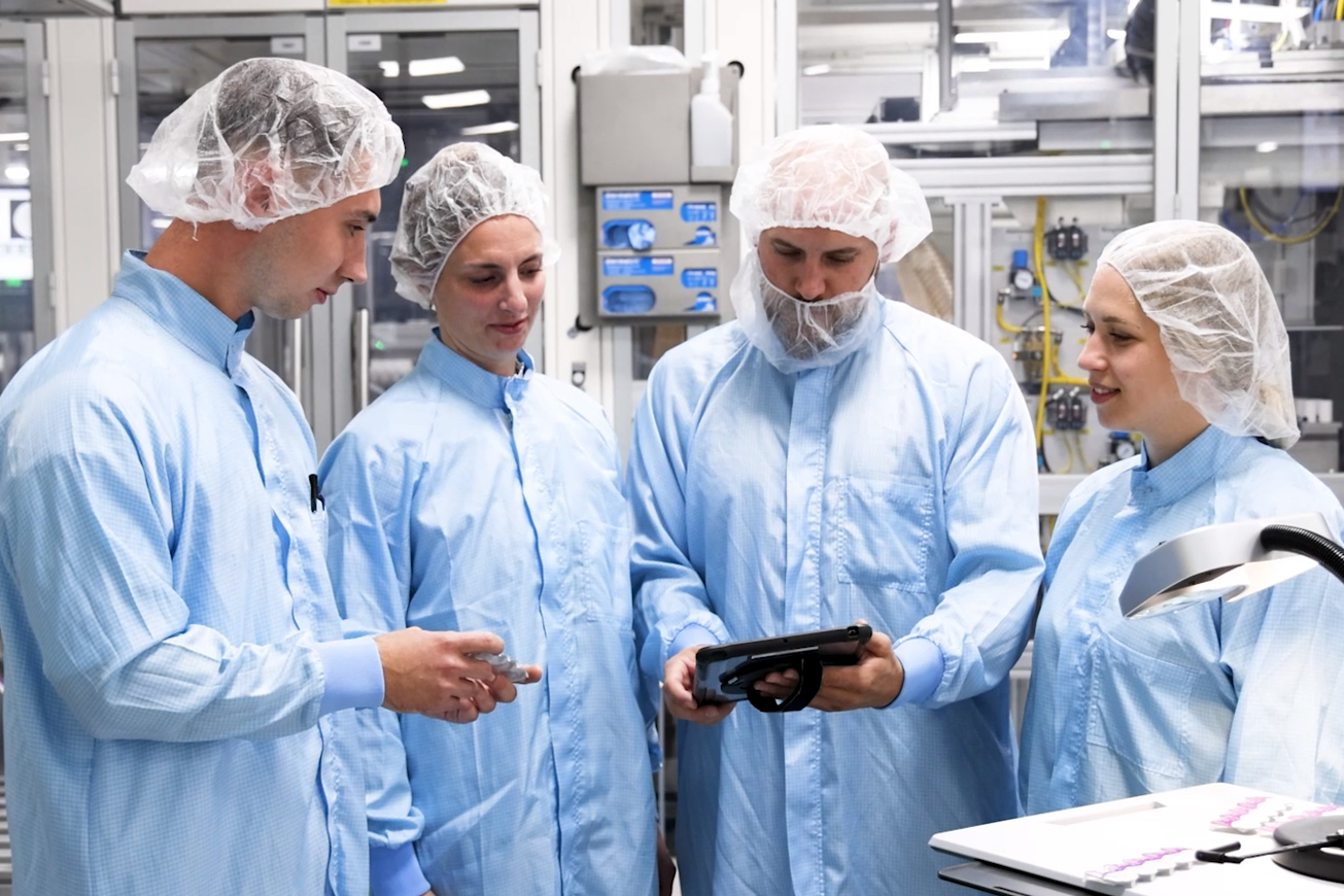Vier Labortechniker in Schutzkleidung betrachten ein Tablet.