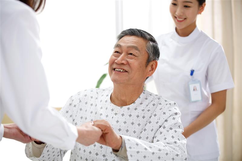 Smiling man in operating gown holding hands with doctor with nurse behind him