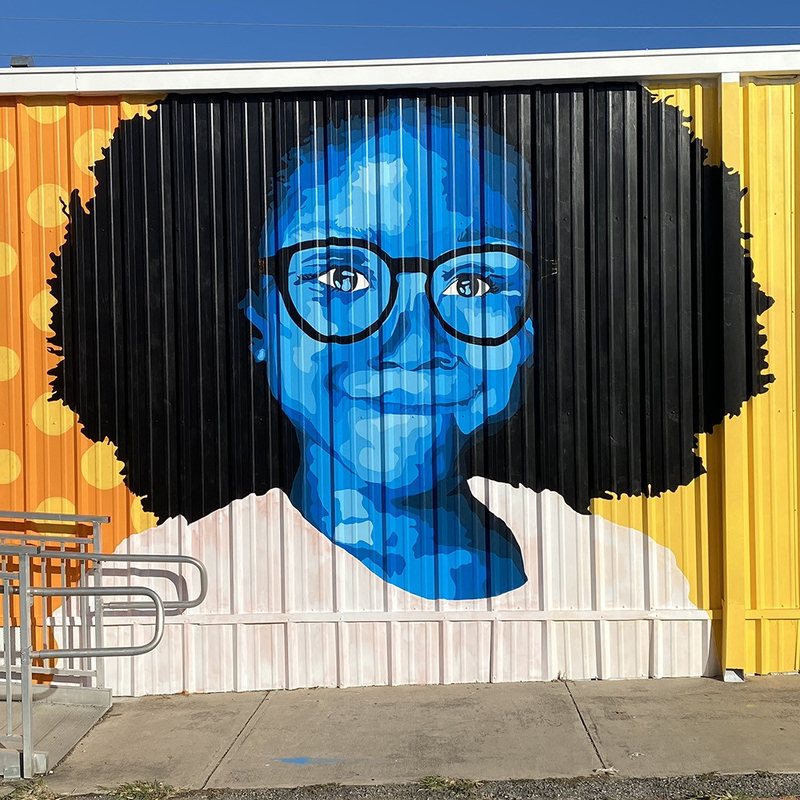 Painted mural on side of building showing a smiling girl wearing glasses