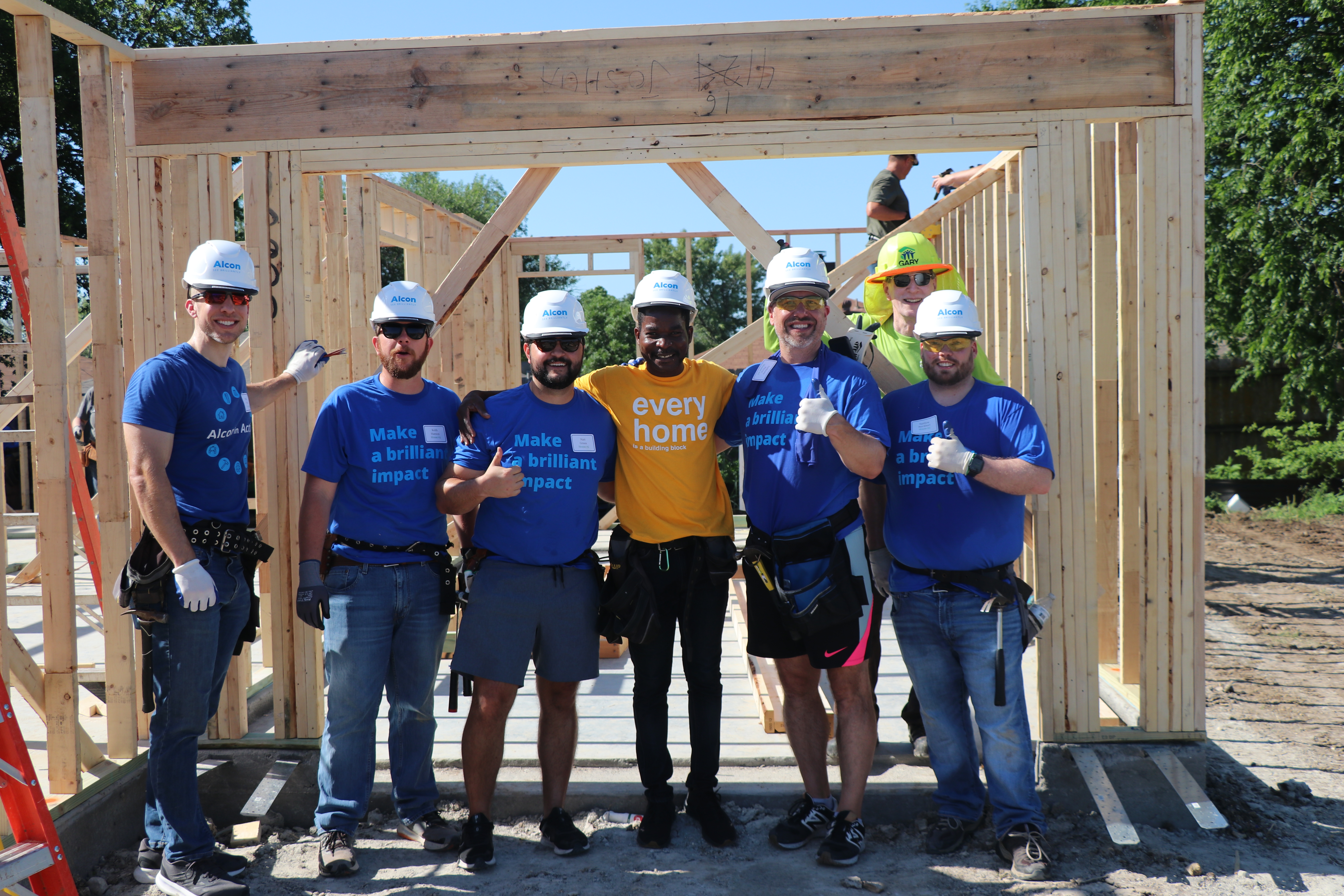 Group of Alcon volunteers stand in front of frame of house being built