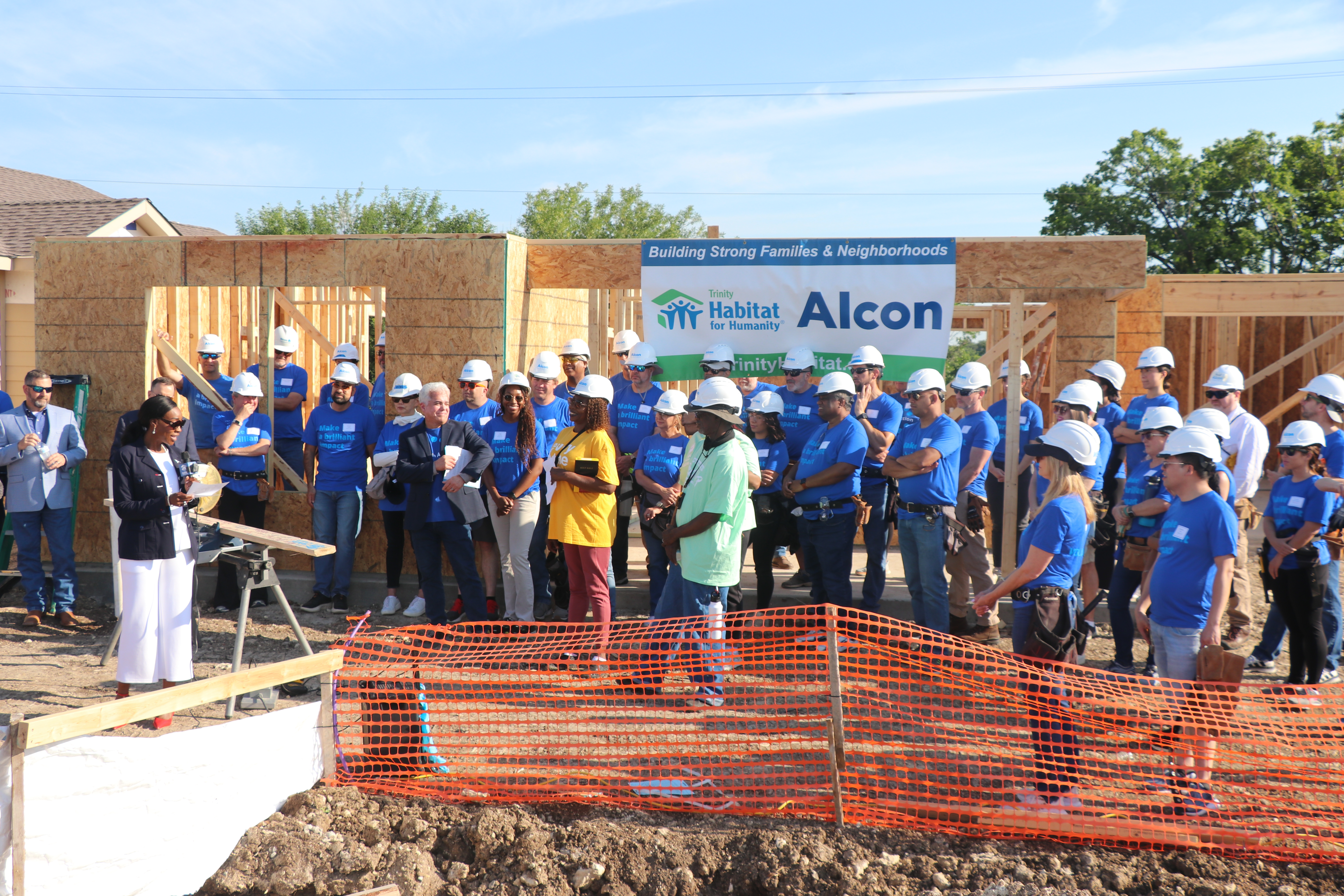 Large group of Alcon volunteers in blue t-shirts standing in front of house being built