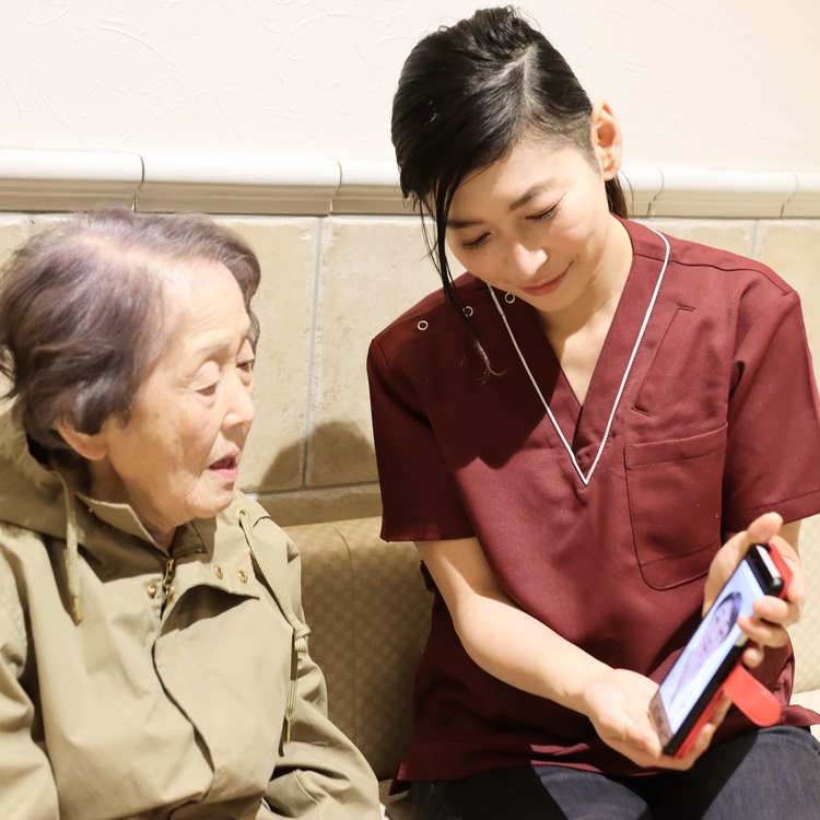 Young woman holds a phone up for an older woman who is on a video call with a medical professional