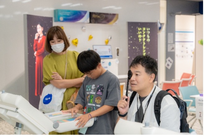 近代的な廊下で、白いシャツを着た男性とグレーのシャツを着た少年が、視力検査を受けながらデジタルディスプレイを見ています。