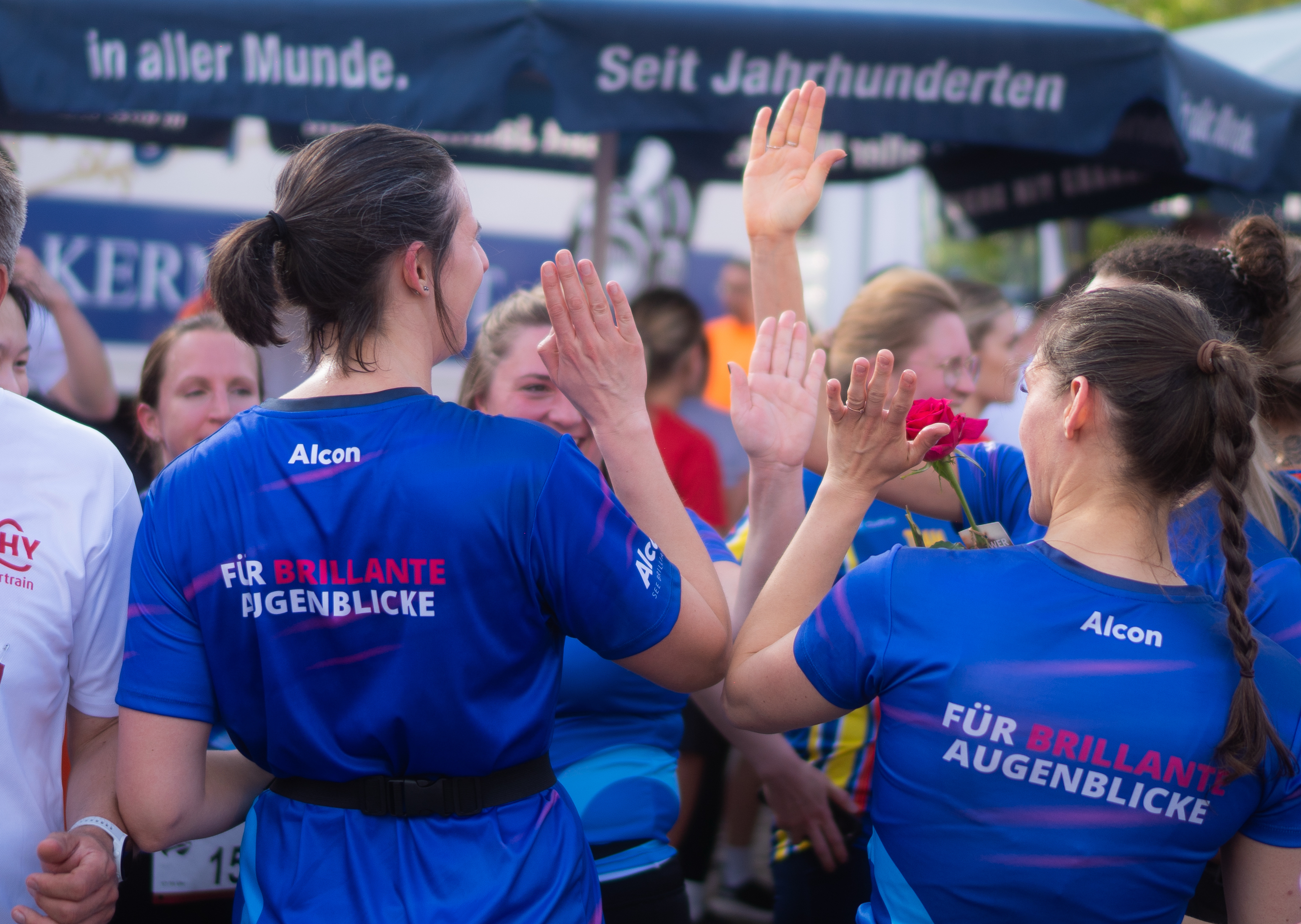 Vier Frauen in blauen Alcon-Shirts klatschen sich gegenseitig ab.