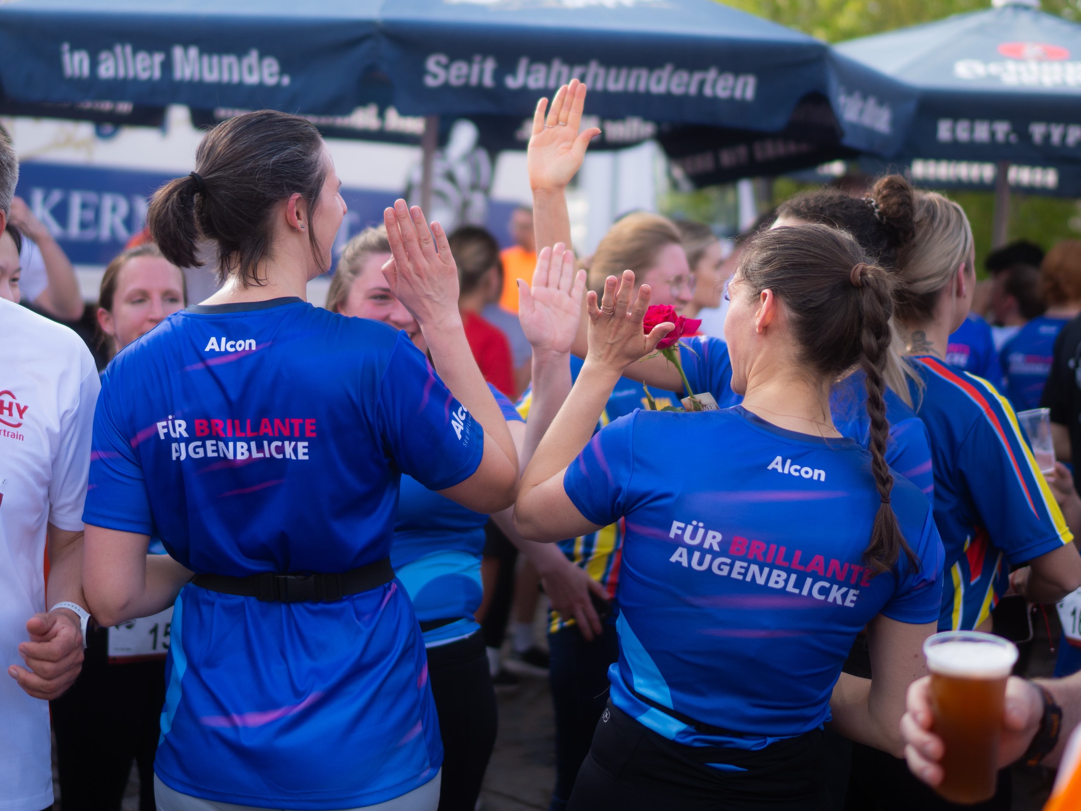 Vier Frauen in blauen Alcon-Shirts klatschen sich gegenseitig ab.