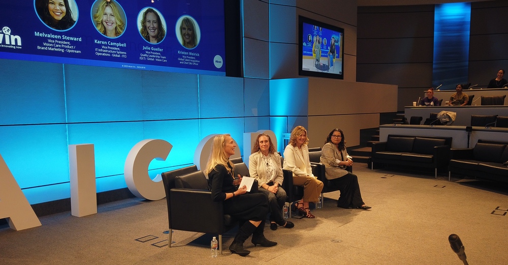 Four women sitting in chairs on stage at conference