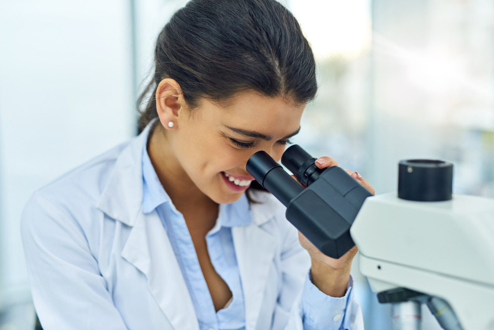 Woman smiling while looking through microscope.