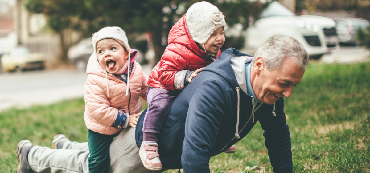 Older man with 2 small children riding on his back.