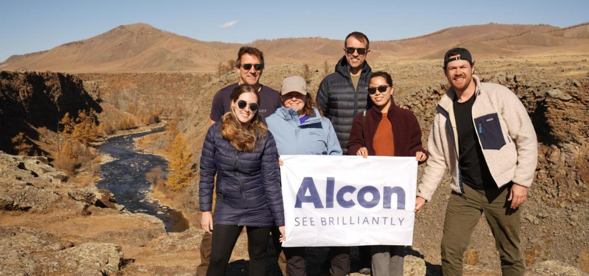 Alcon volunteers standing in group outside, holding sign that says "Alcon - see brilliantly"