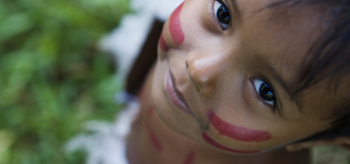 A child's face with red painted stripes on the cheeks is looking upward.
