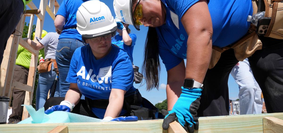 Closeup of Alcon volunteers in blue shirts helping to build the frame of a new home
