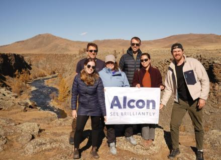 Alcon volunteers standing in group outside, holding sign that says "Alcon - see brilliantly"