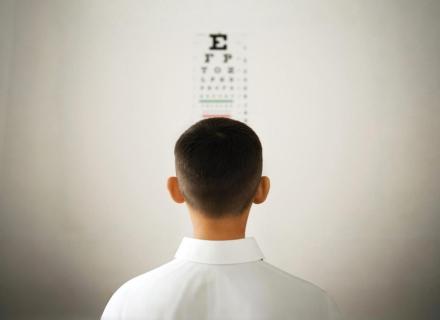 Man in a white shirt is looking at an eye chart.