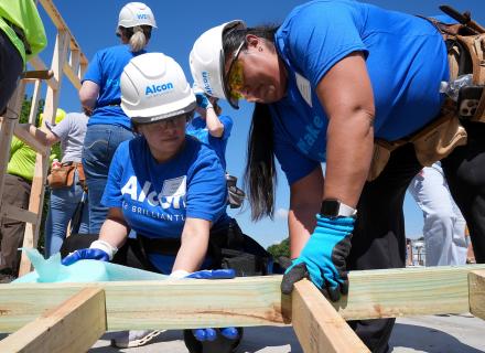 Closeup of Alcon volunteers in blue shirts helping to build the frame of a new home