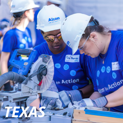Image of an Alcon volunteers in blue Alcon t-shirts and hard hats doing construction work in Texas