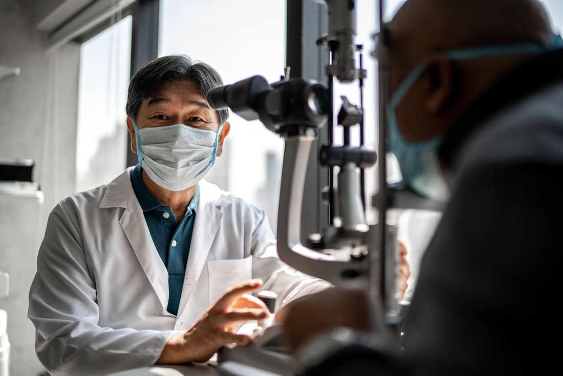 Medical professional in lab coat and mask conducting eye exam with equipment
